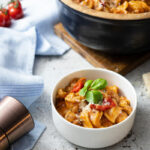 Schüssel mit Tortellini in Tomatensauce, garniert mit frischem Basilikum, daneben Pfeffermühle und Cocktailtomaten.