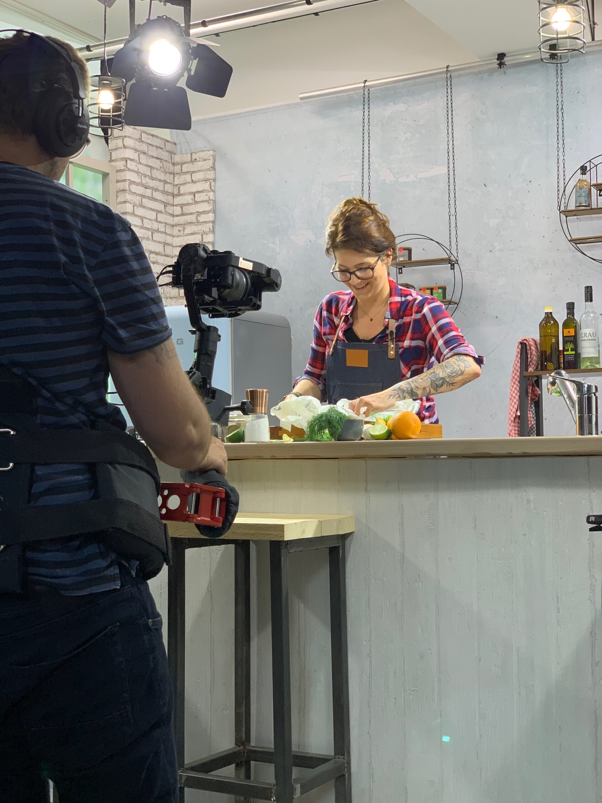 Koch dreht in einer Küche ein Video, während ein Kameramann mit Steadicam filmt. Verschiedene Zutaten liegen auf dem Tresen.