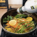 Öl wird in eine Pfanne mit Gemüse, Zitronenscheiben und Kräutern gegossen.