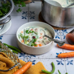 Hausgemachte rheinische Bohnensuppe mit Buttermilch, Kartoffeln und grünen Bohnen in einem Topf, serviert mit Karotten