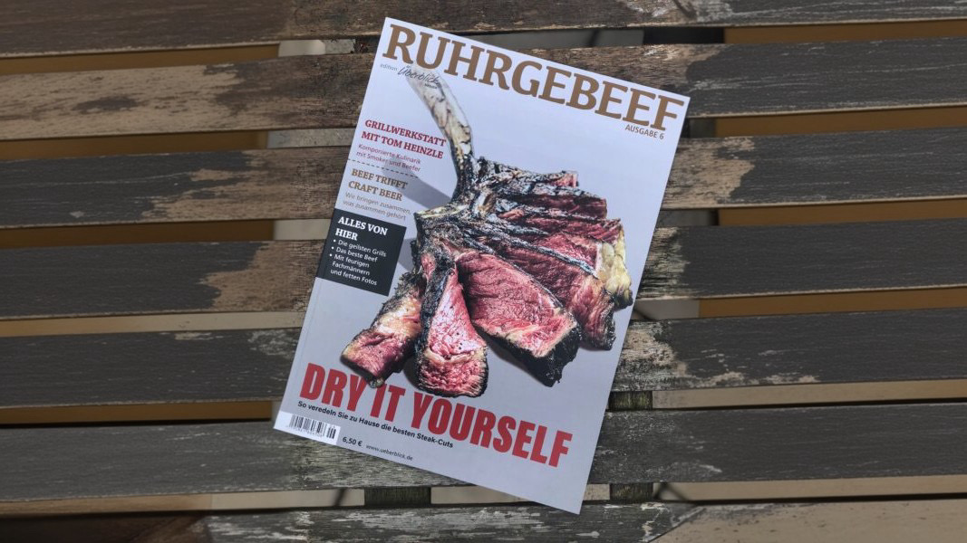 Zeitschrift über Grillen und Fleischzubereitung auf einer Holzbank, zeigt ein großes Stück rohes Fleisch.