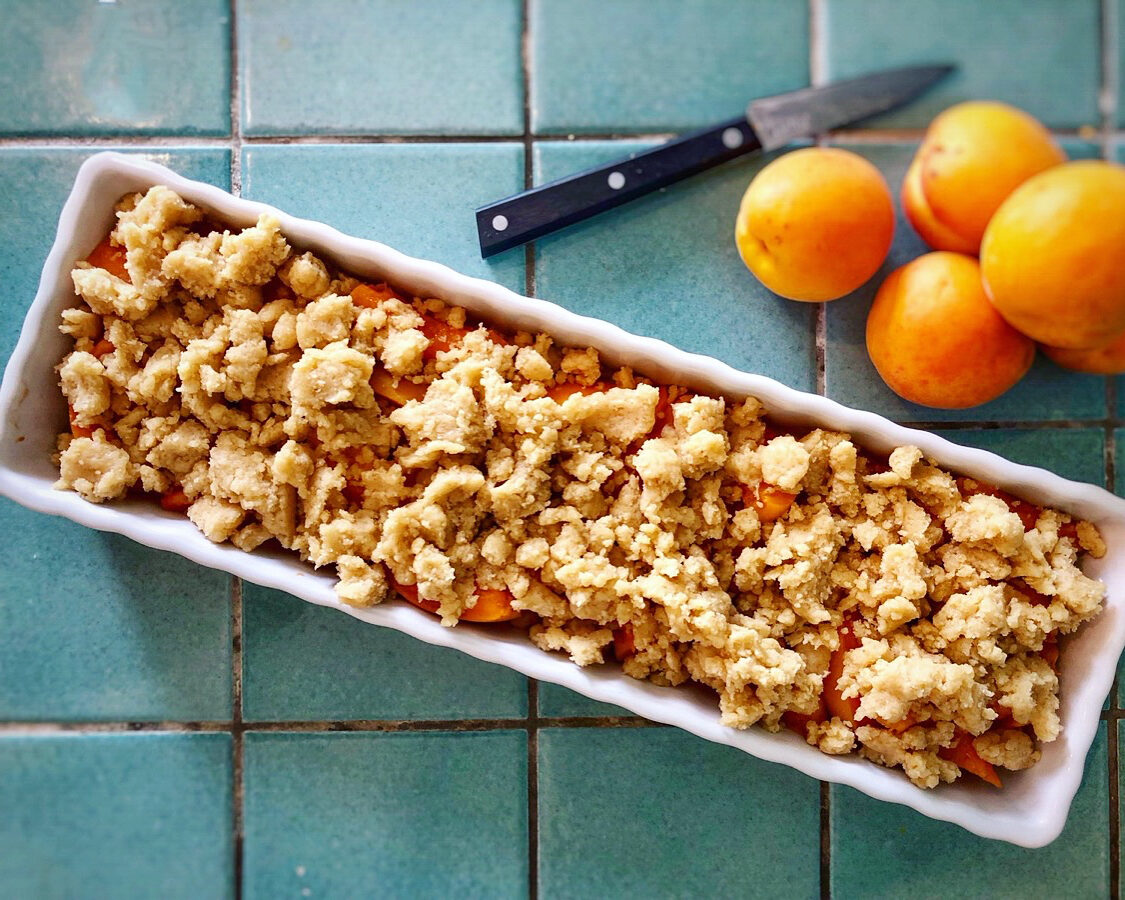 Aprikosen-Crumble-01 Birnenaufläufe in weißen Förmchen mit karamellisierter Kruste, darauf poelierte Birnenhälften. Im Hintergrund weitere Birnen.