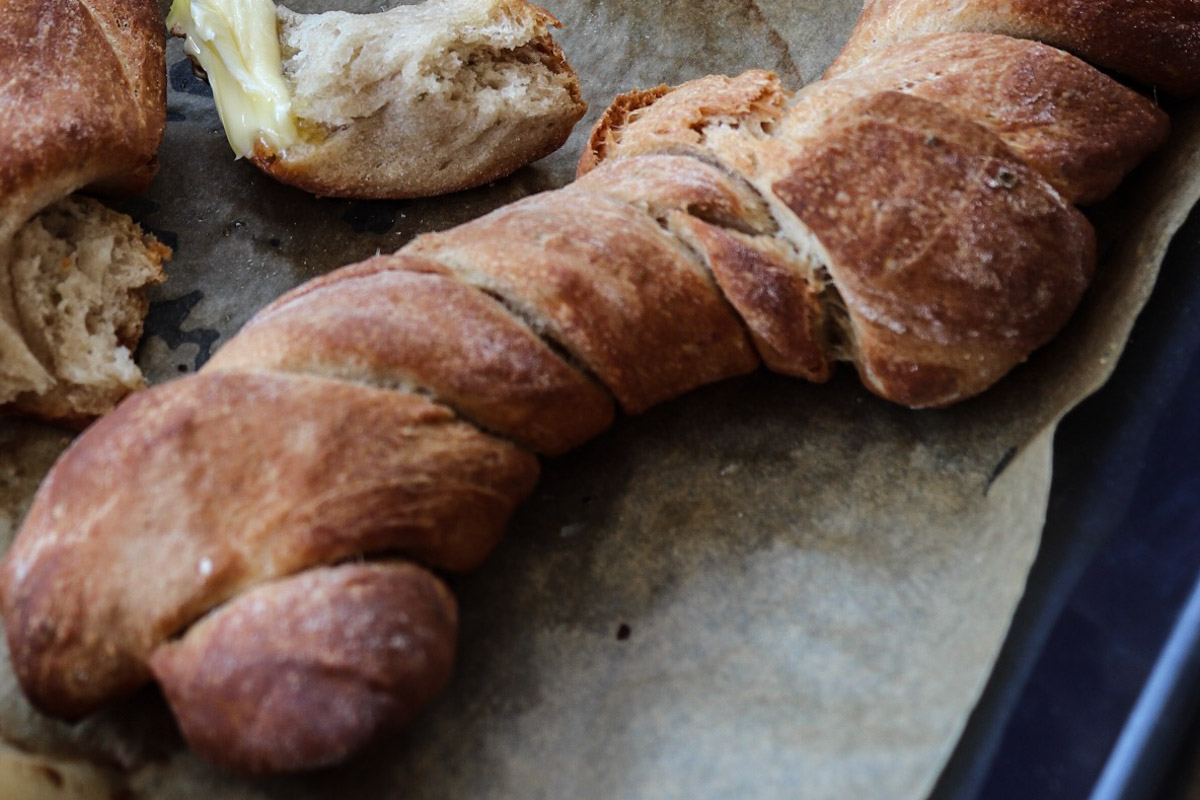 Gebackenes, gedrehtes Brot auf Backpapier mit einem Stück, aus dem geschmolzener Käse fließt.