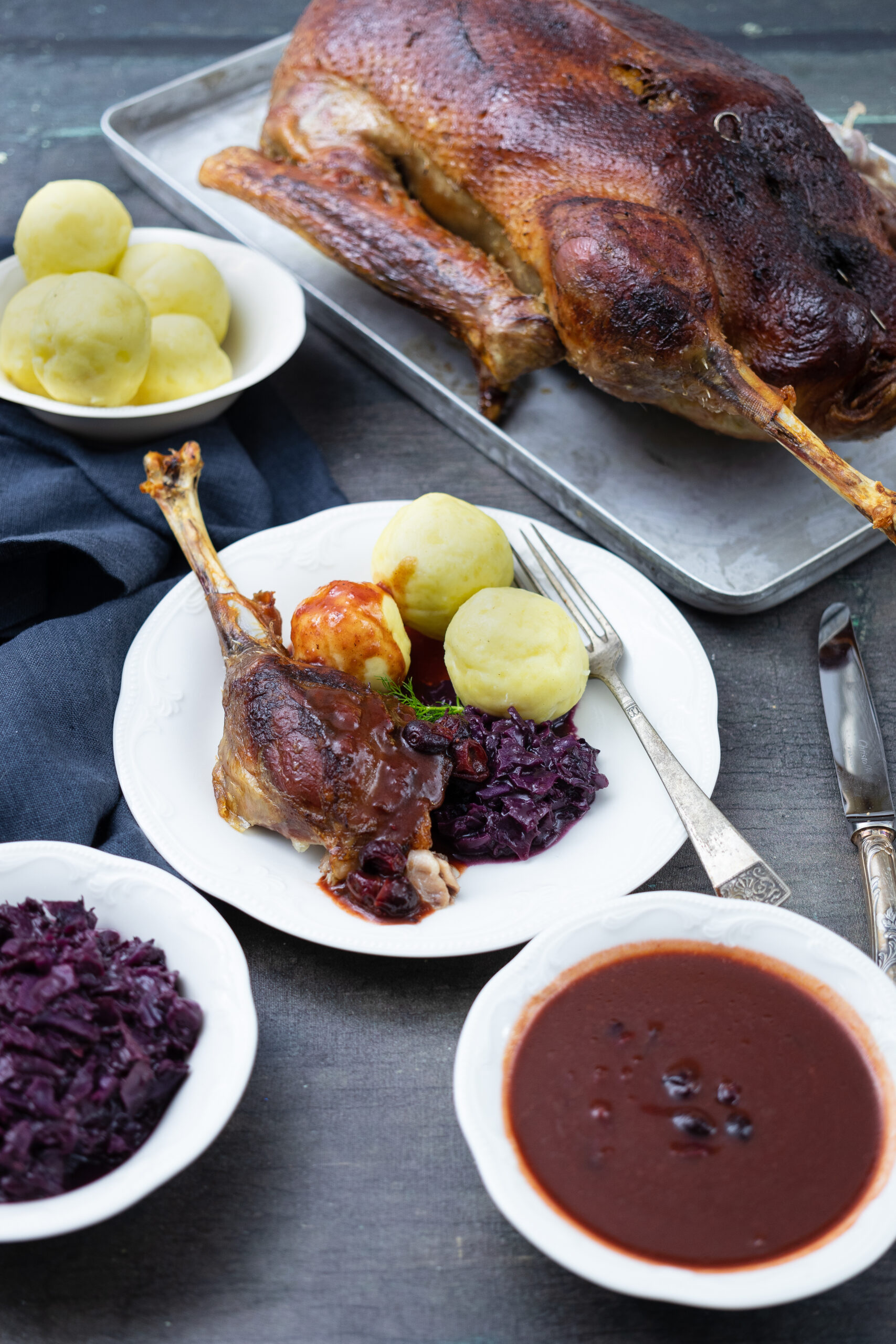 Gebackene Ente auf Blech, angerichtet mit Rotkohl, Kartoffelknödeln und Sauce auf einem Teller.