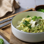 Schüssel mit Nudeln, grünem Pesto, Feta, Pinienkernen und frischen Kräutern auf einem Holzbrett.