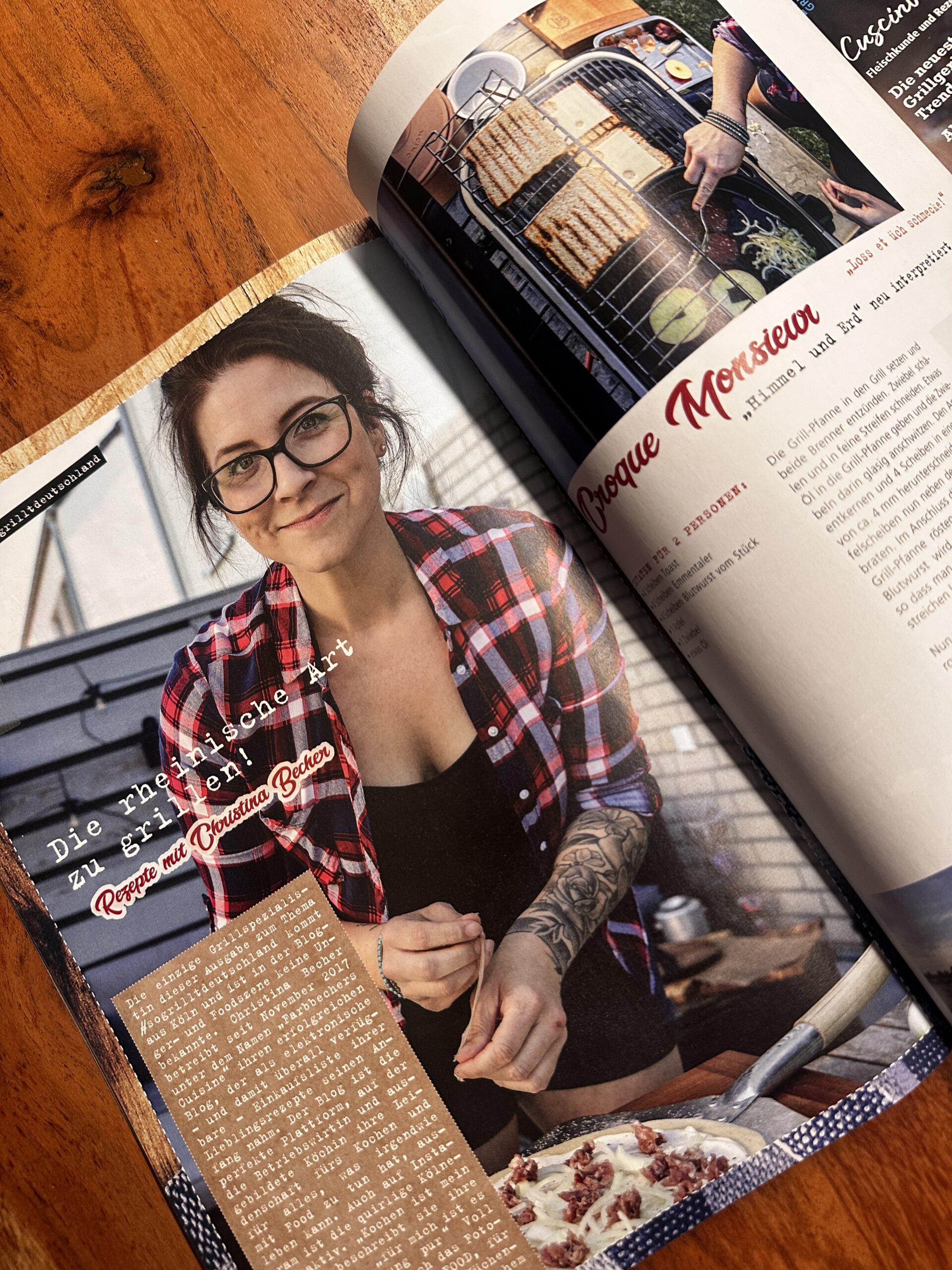 fire&Food-3 Frau in kariertem Hemd beim Kochen, daneben Rezeptseite in aufgeschlagenem Magazin auf Holztisch.
