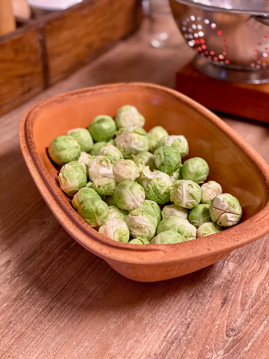 Rosenkohl_aus_dem_römertopf_2 Rosenkohl in einer braunen Keramikschale auf Holztisch, im Hintergrund Teil eines Siebs sichtbar.