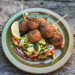 Falafel auf grünem Salat mit Zitronenscheibe, angerichtet auf einem Teller mit rustikalem Holzuntergrund.