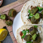Zwei gefüllte Wraps mit grünen Falafelbällchen, Koriander, Käse und Zitrone auf einem Teller.
