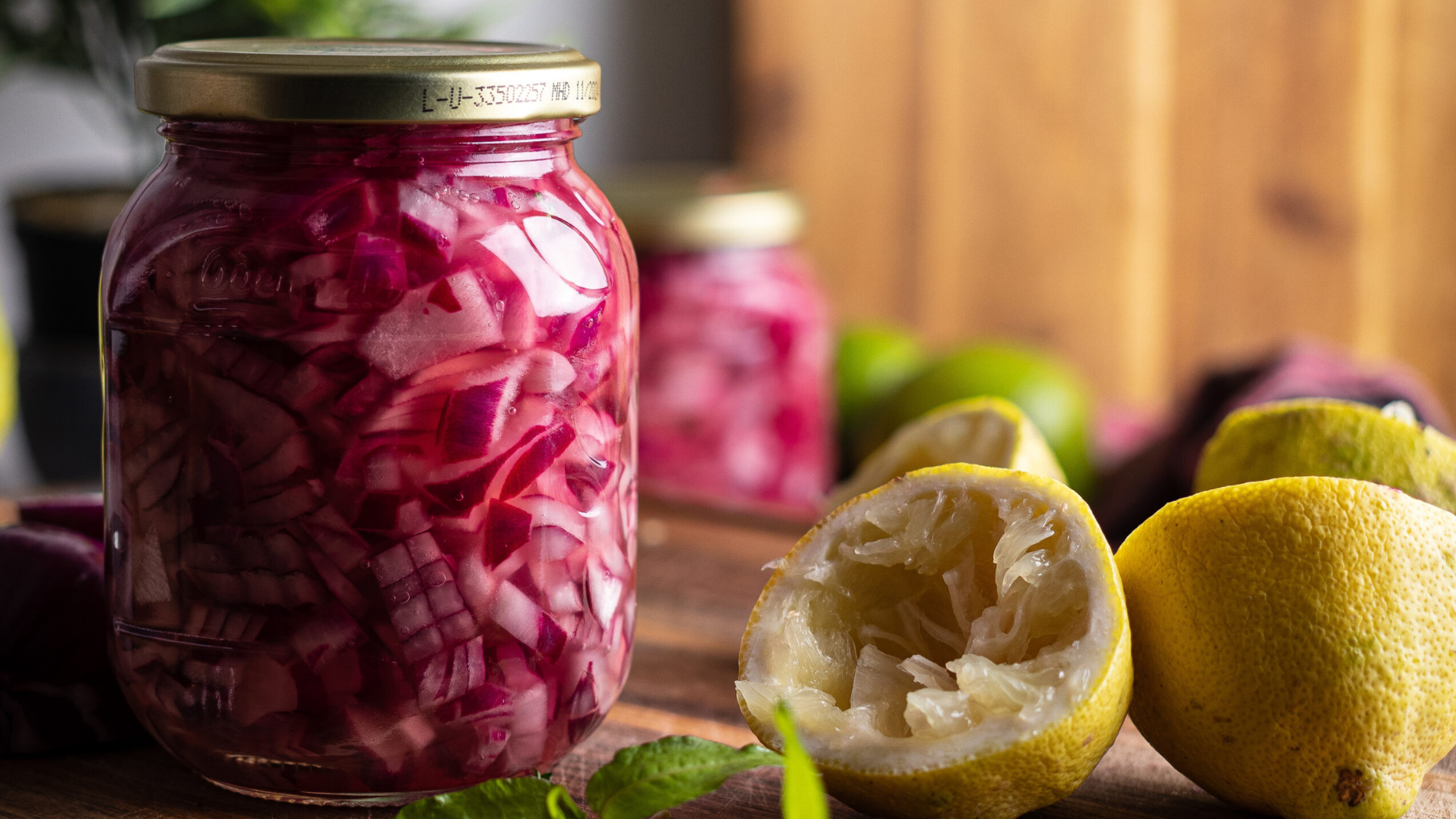 Ein Glas mit eingelegten roten Zwiebeln neben ausgepressten Zitronen auf einem Holztisch.