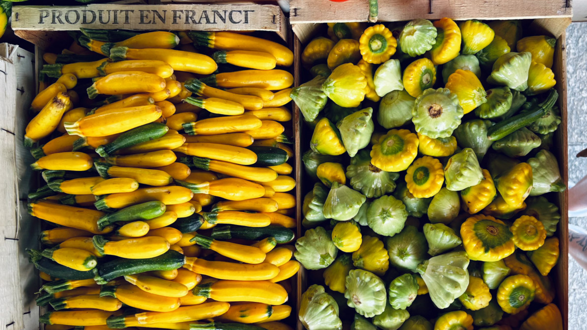 Holzkisten mit gelben Zucchini links und Patty Pan Kürbissen rechts, auf einem Markt ausgestellt.