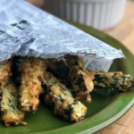 Frittierter Zucchinisticks in Zeitungspapier gewickelt auf einem grünen Teller.