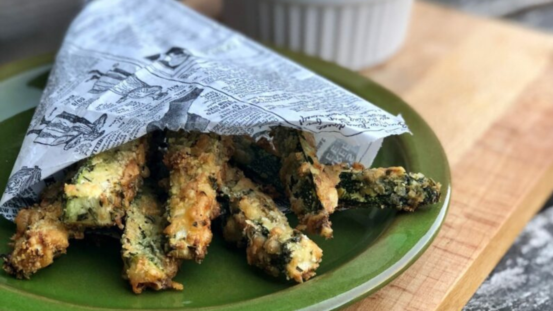 Frittierter Zucchinisticks in Zeitungspapier gewickelt auf einem grünen Teller.