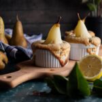 Zwei Birnen-Küchlein in Förmchen auf Holzbrett, umgeben von Birnen und Zitronenhälfte, rustikaler Hintergrund.