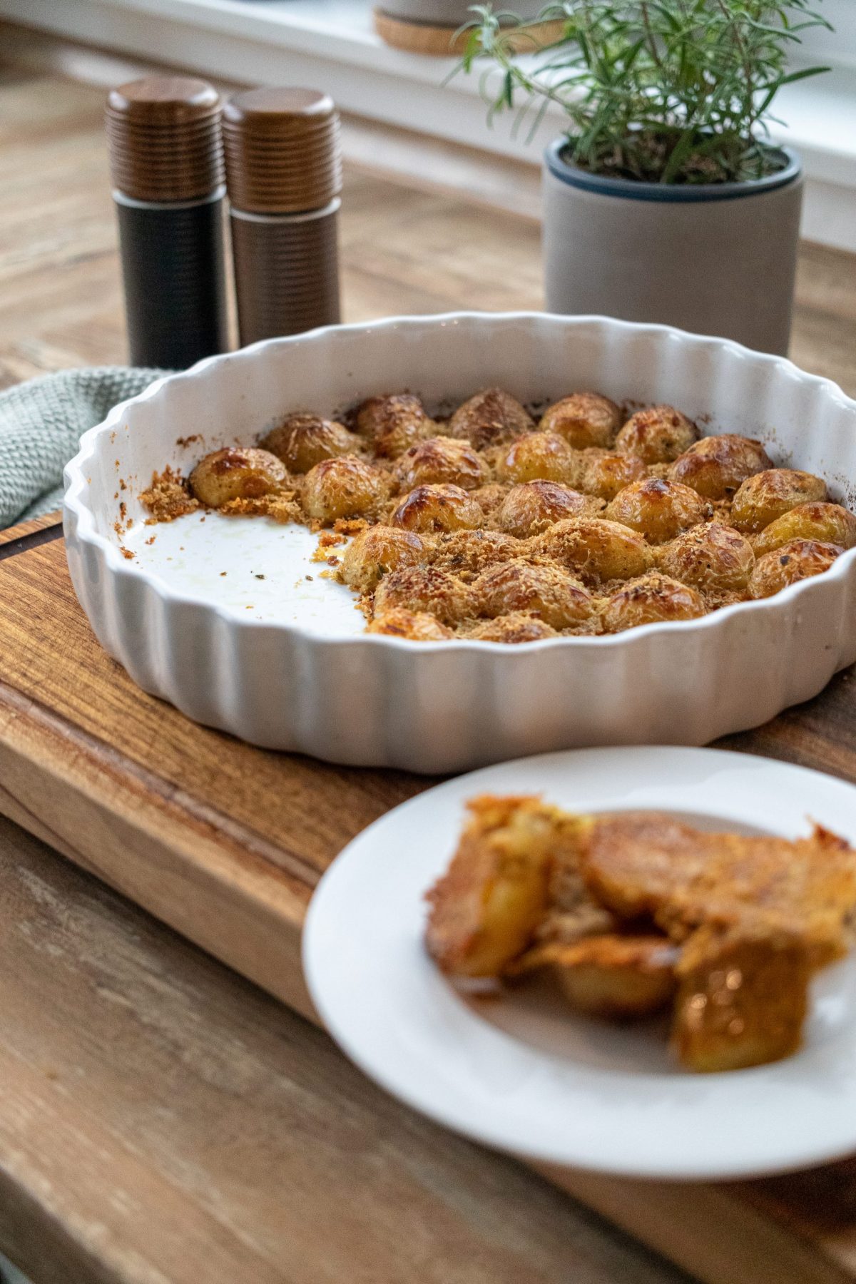 Ofenfrische Kartoffeln mit knuspriger Kruste in einer runden weißen Backform auf Holzbrett serviert.