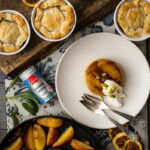 Rustikale Obstkuchen in kleinen Formen, ein Teller mit Apfel-Dessert und Sahne, daneben gebratene Apfelscheiben in Pfanne.