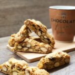 Biscotti mit Mandeln auf Holzbrett, daneben eine Kaffeetasse auf Holztisch.