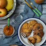 Gebratene Apfelringe auf Teller mit Gabel, Apfelmarmelade im Glas, Zimt-Zucker-Mischung, Äpfel und Zitrone in Holzschale.