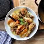 Ein Teller gebratener Hähnchenkeulen mit Orangen und Kräutern, daneben ein Topf und ein Küchenhandtuch.