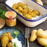 Gebackene Kartoffeln in einer Ofenform, daneben Currygewürz und ein Teller mit Kartoffeln und Joghurt-Dip.