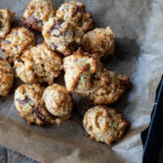 Frische Schokoladenkekse auf einem Backblech mit braunem Backpapier, von oben fotografiert.