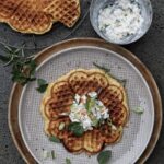 Herzhafte Waffel mit Frischkäse-Dip und Kräutern auf einem Teller, daneben eine separate Schüssel mit Dip.