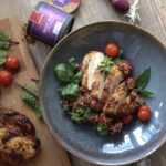 Gegrilltes Hähnchen auf Quinoa mit Tomaten und Kräutern in einer Schale, daneben Gewürzglas und Frühlingszwiebel.