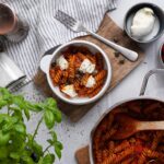 Schale mit Tomatensauce-Fusilli und Käse, daneben Topf, Basilikum, Salz, Pfeffer, Kirschtomaten und Mozzarella.