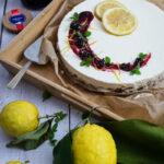 Zitronenkuchen dekoriert mit Zitronenscheiben, Beeren und Minze auf Holztablett, daneben ein Glas mit Beerenkonfitüre.
