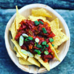 Schale mit Tortillachips, bedeckt mit Tomatensalsa und grünen Zwiebeln auf einem Holztisch.