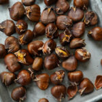 Geröstete Maronen liegen auf einem Backblech, einige sind geöffnet, mit sichtbaren Schalen und goldbraunem Kern.
