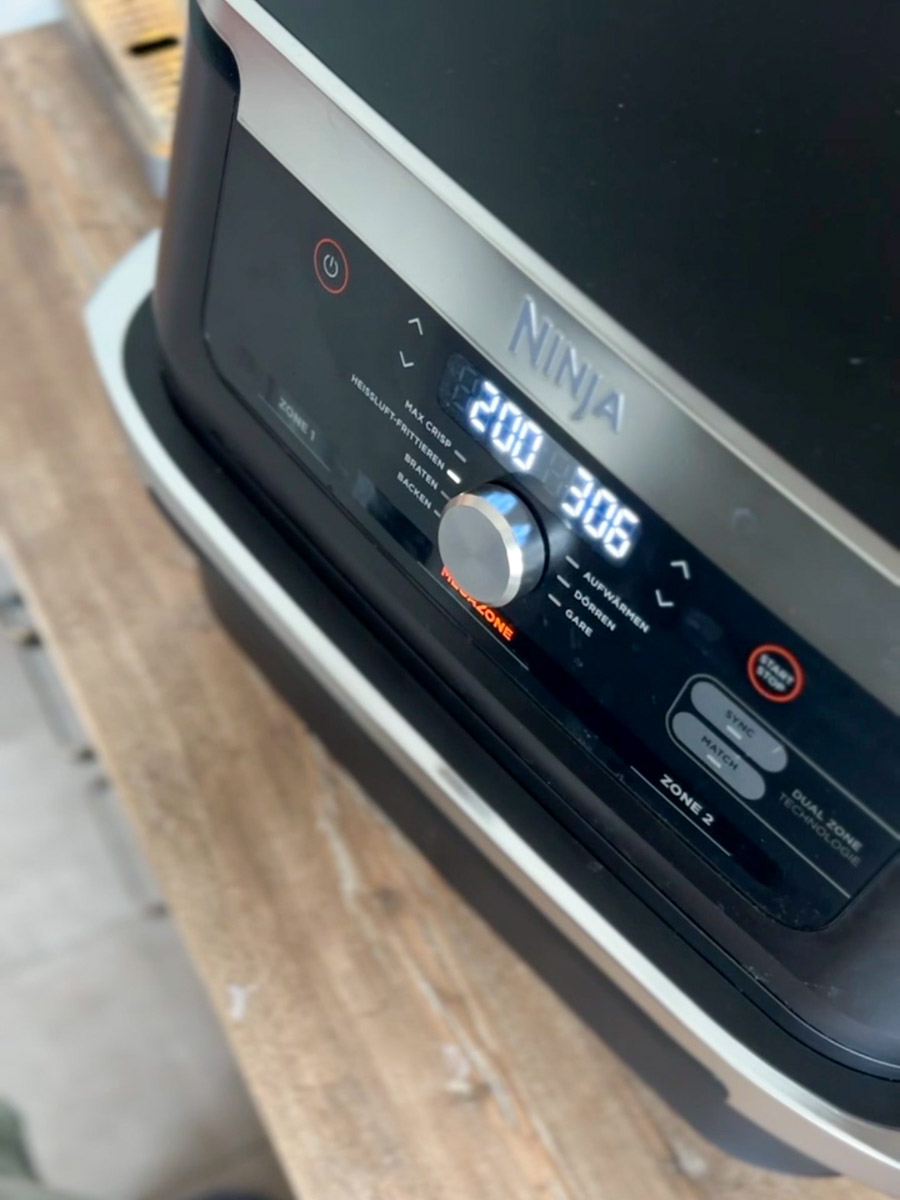 Display einer Heißluftfritteuse mit Temperaturen von 200 und 306 Grad auf einem Holztisch.