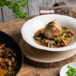 Knödel mit Pilzragout und Kräutern in einer Schale, daneben Pfanne mit Ragout und frische Petersilie.