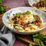 Nudeln mit Hackfleisch, Joghurt und Minze in einer Schale auf einem Holzbrett, daneben frische Minzblätter.