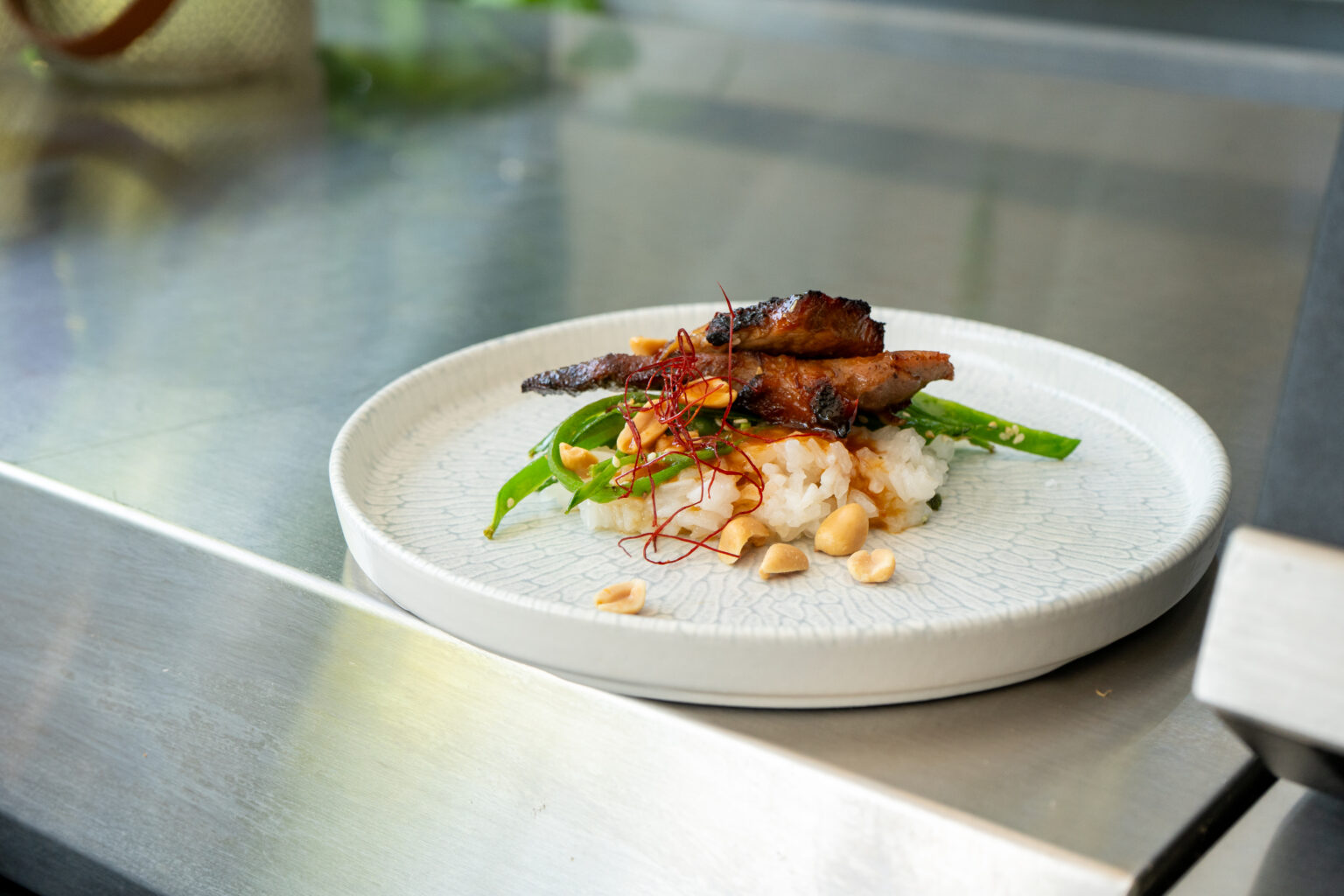 Gericht mit Reis, gegrilltem Fleisch, grünen Bohnen und Erdnüssen auf weißem Teller, dekoriert mit roten Fäden.