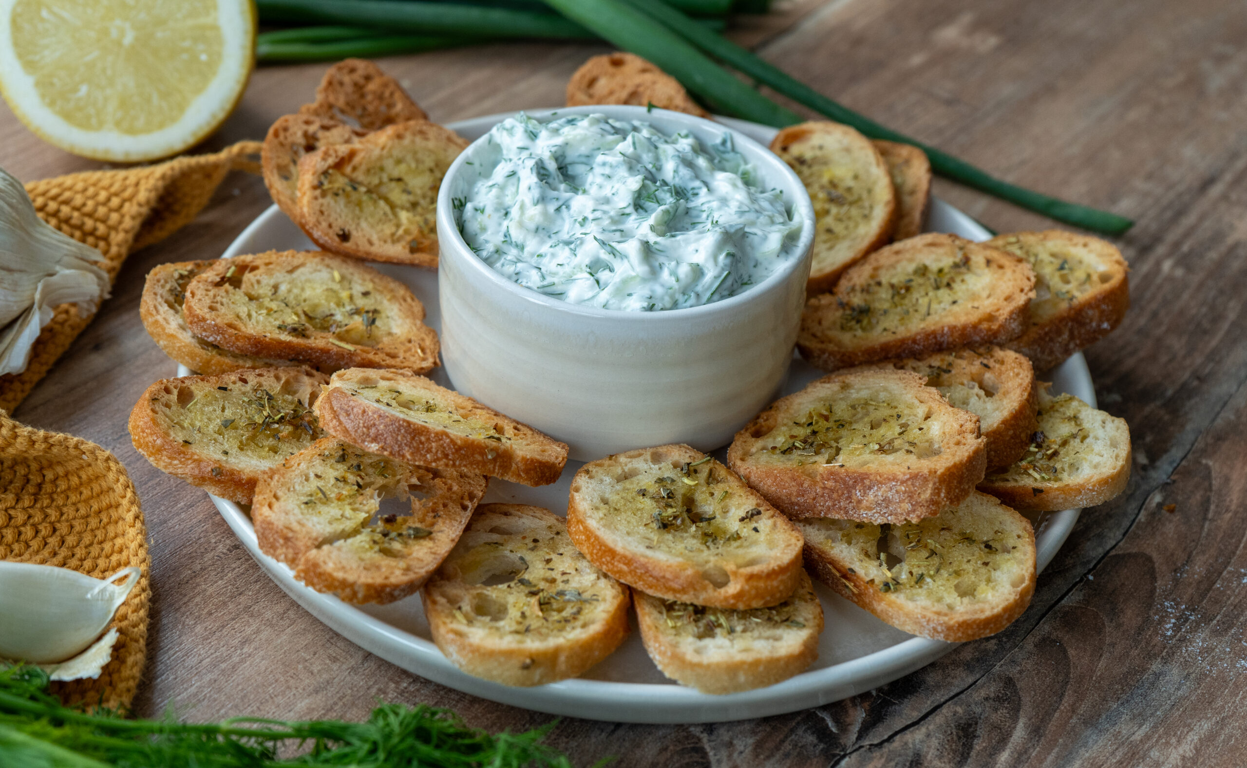 Selbstgemachter Tzatziki-Dip mit frischer Gurke und Dill, serviert mit knusprigen Brotchips aus Brötchen – angerichtet auf einem weißen Teller