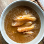 Schale mit mariniertem Hühnerfleisch in einer dunklen Flüssigkeit auf einem hölzernen Untergrund.