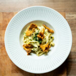 Pasta mit Pfifferlingen und Kräutern in einem weißen Teller auf einem Holztisch.