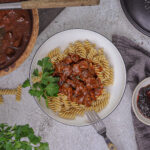 Rindergulasch im Römertopf serviert – zart geschmortes Rindfleisch in dunkler Soße mit Zwiebeln, Rotwein und Balsamico, angerichtet in rustikaler Schale.
