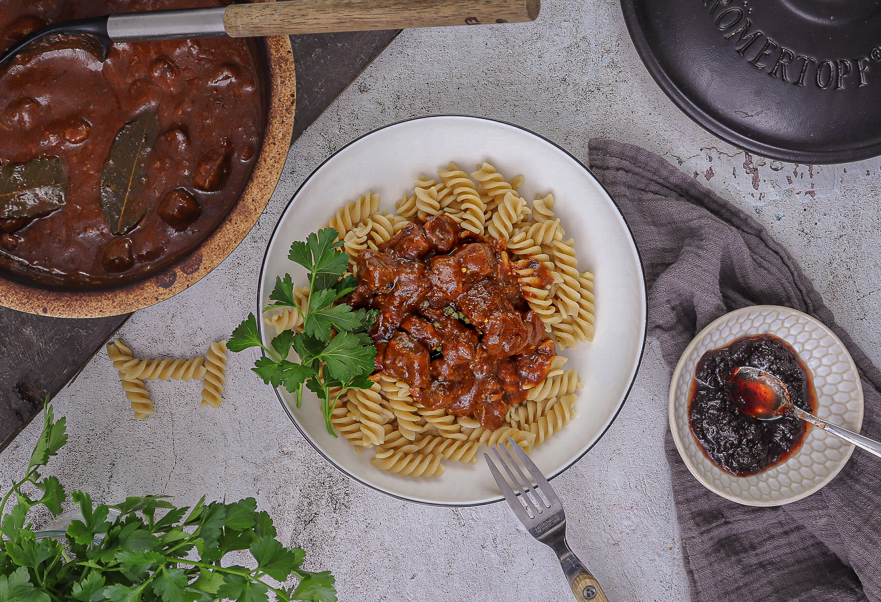 Rindergulasch im Römertopf serviert – zart geschmortes Rindfleisch in dunkler Soße mit Zwiebeln, Rotwein und Balsamico, angerichtet in rustikaler Schale.