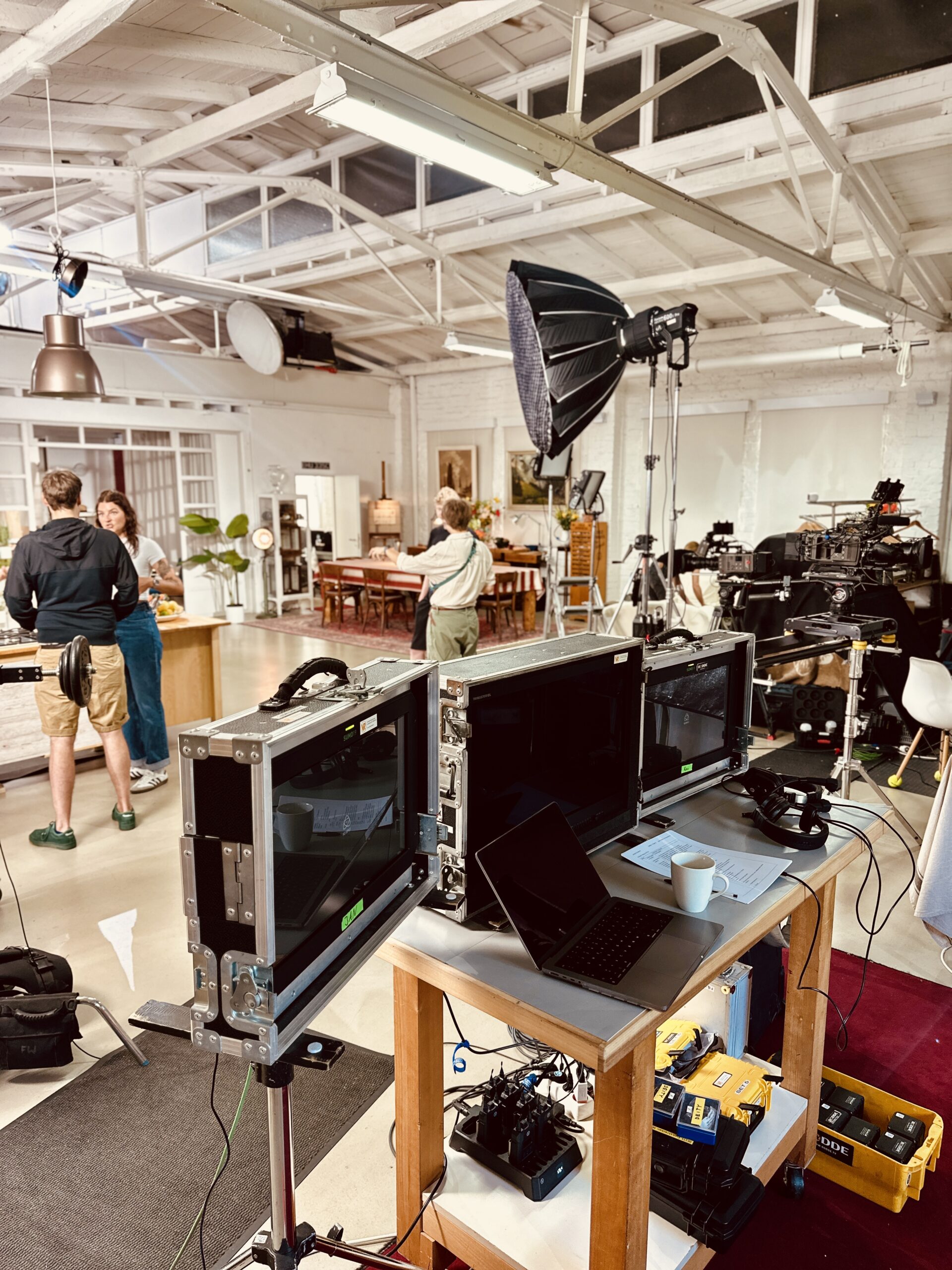 einfach-&-köstlich-2 Filmstudio mit Kameras und Monitoren auf Stativen. Menschen im Hintergrund bereiten eine Szene vor.
