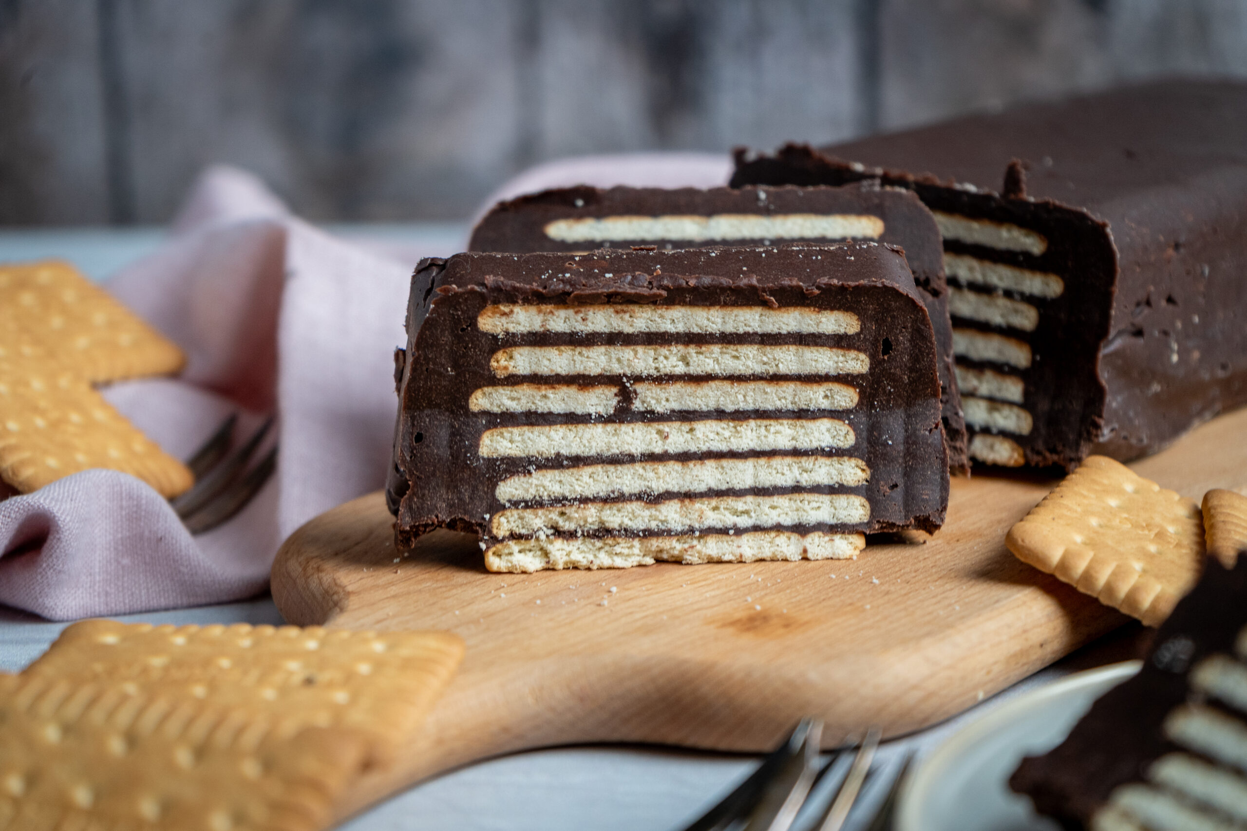 Schokoladenkuchen mit Keksschichten, auf einem Holzbrett angerichtet, umgeben von einzelnen Keksen.