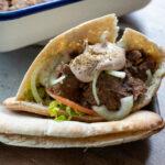 Gefülltes Pita mit Fleisch, Zwiebeln, Tomaten und Sauce, auf einem Tablett serviert, im Hintergrund eine Auflaufform.