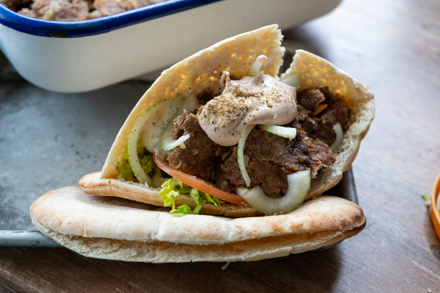 Gefülltes Pita mit Fleisch, Zwiebeln, Tomaten und Sauce, auf einem Tablett serviert, im Hintergrund eine Auflaufform.