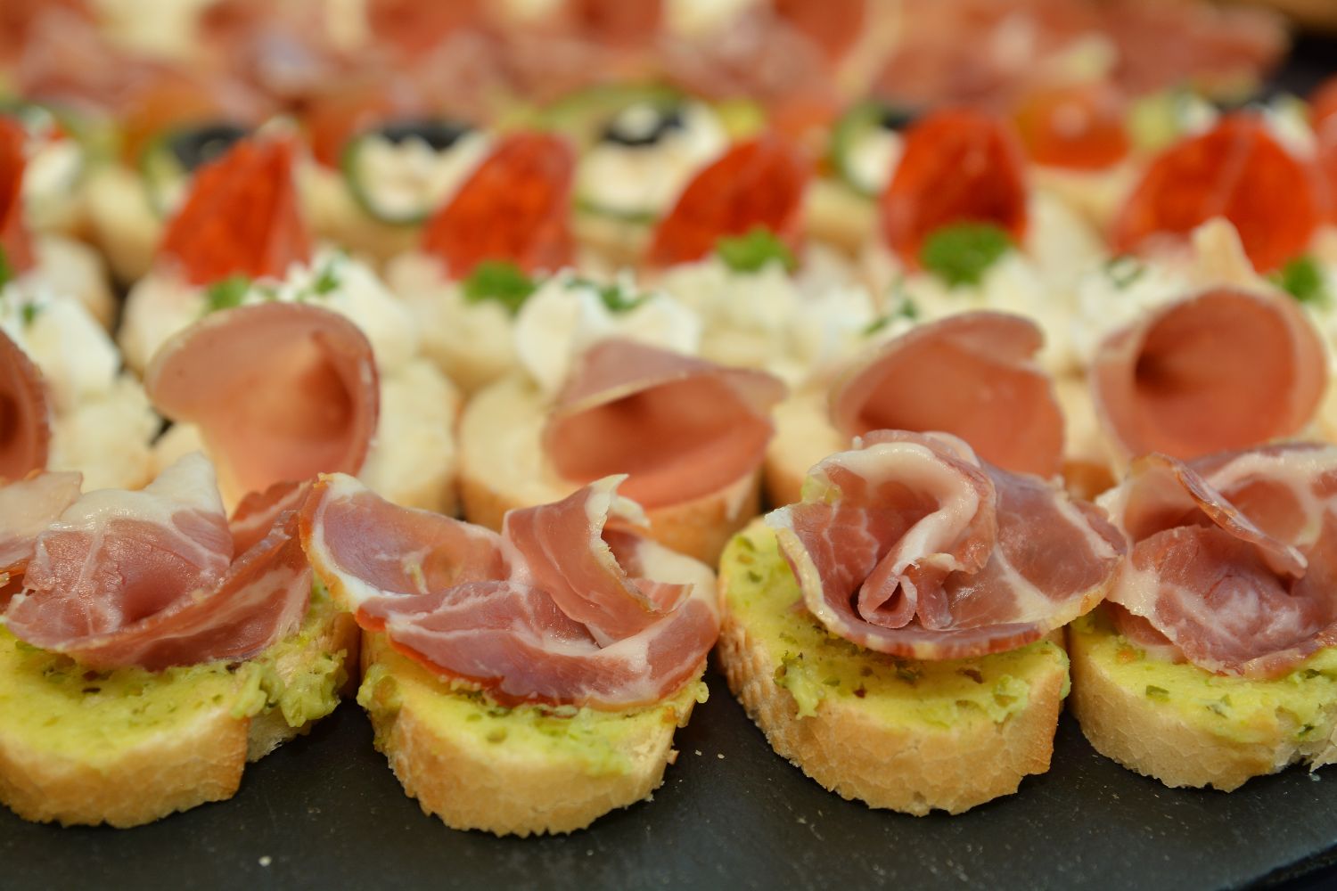 Vorspeisen mit Schinken, serviert auf Baguette-Scheiben, dekoriert mit weiteren delikaten Zutaten auf Platten.