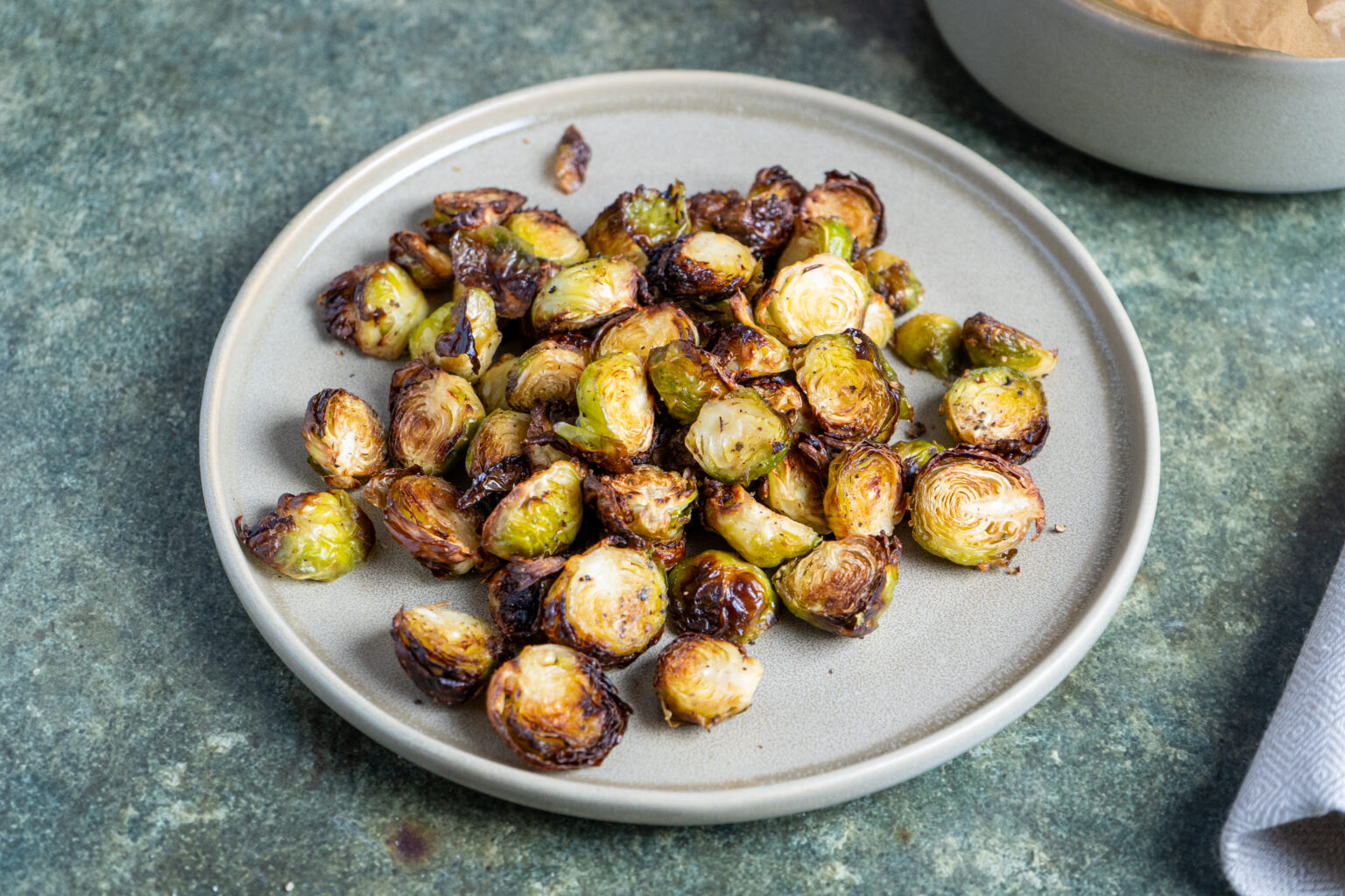 Gerösteter Rosenkohl auf einem grauen Teller, auf grünlicher Oberfläche serviert.