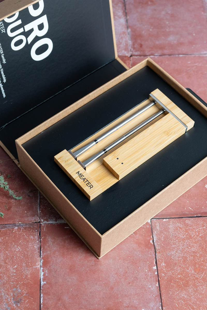 Kabelloses Fleischthermometer in edler Holzhalterung, im offenen Karton auf einem terrakottafarbenen Boden präsentiert.