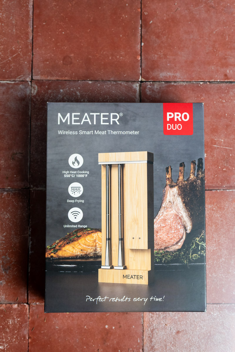 Schachtel eines drahtlosen Smart-Meat-Thermometers auf rotem Fliesenboden, mit Abbildung eines Fleischstücks.