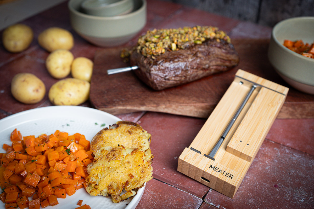 Rinderfilet-04 Gekochtes Rindfleisch mit Kräuterkruste, kleinen Kartoffeln, Karottenwürfeln und einem Thermometer auf einem Tisch.