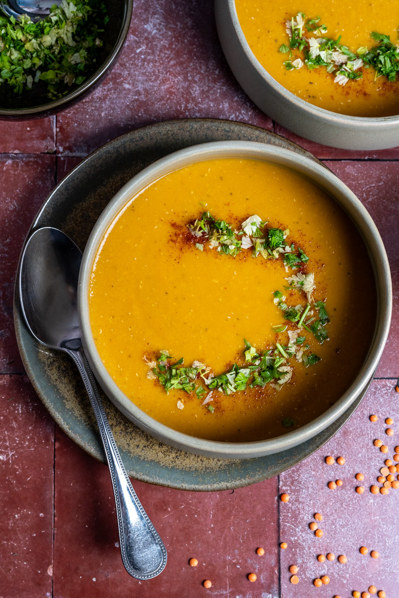 Eine Schüssel mit cremiger Linsensuppe, garniert mit gehackten Kräutern und Gewürzen, daneben ein Löffel.
